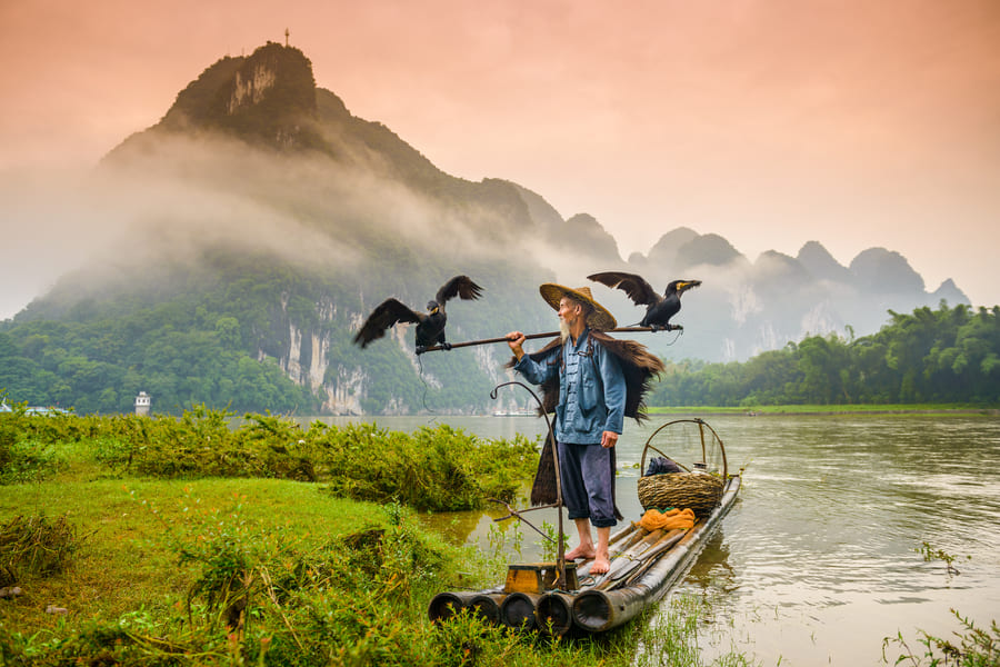 Pescador Cormoran en embarcación en el río chino de Yangshuo